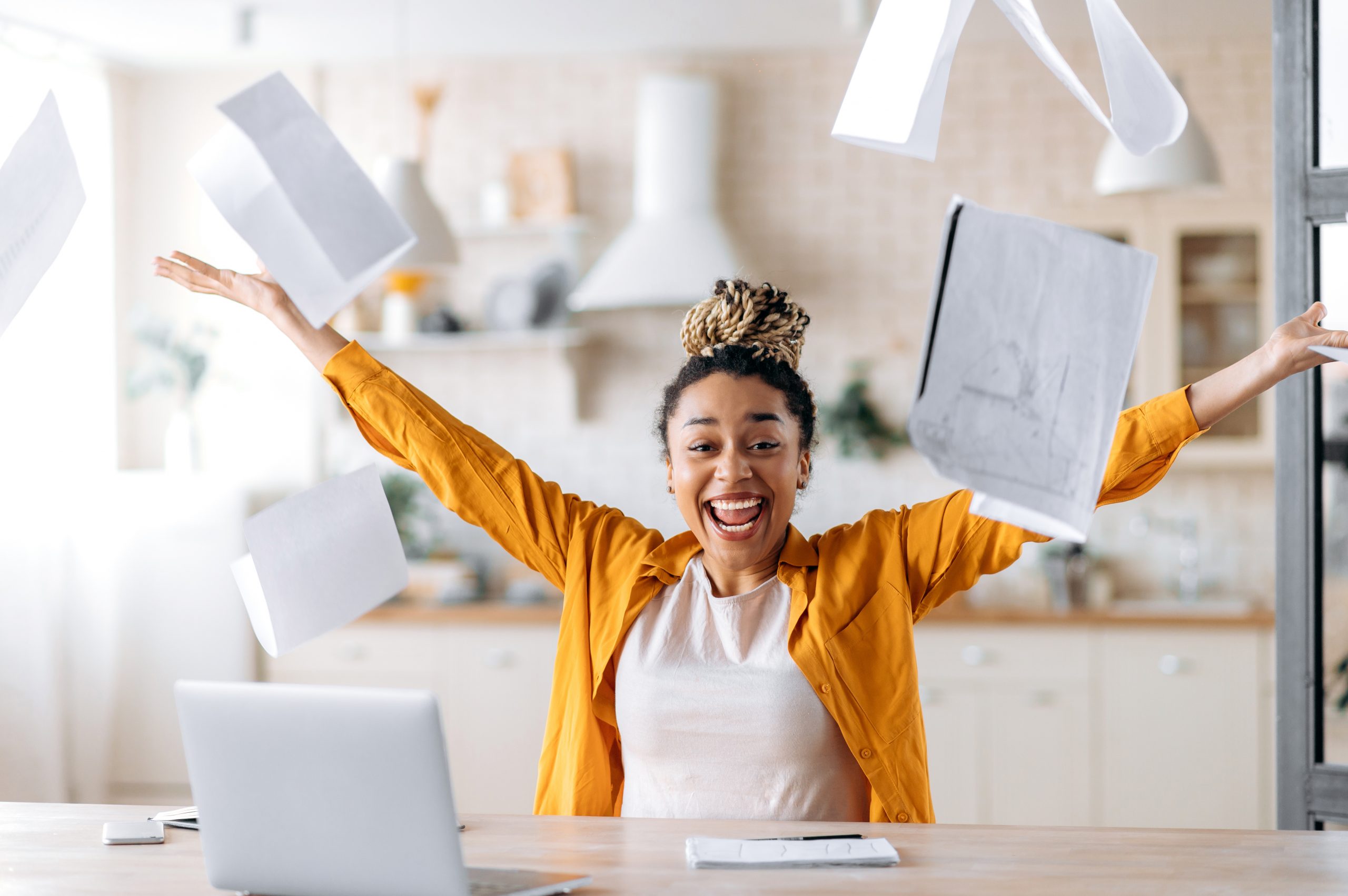 excited happy young african american woman, business lady, manager or freelancer working remotely at home, enjoying career growth or good deal, gesturing with hands, scattering documents